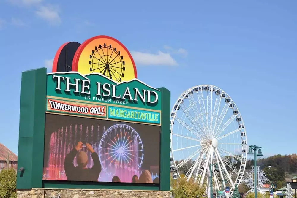 A large green sign for the Island in Pigeon Forge with the wheel in the background