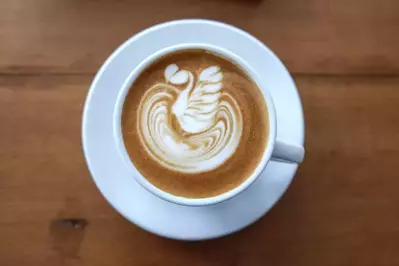 cappuccino with cream on top in a white cup and saucer on a wooden surface